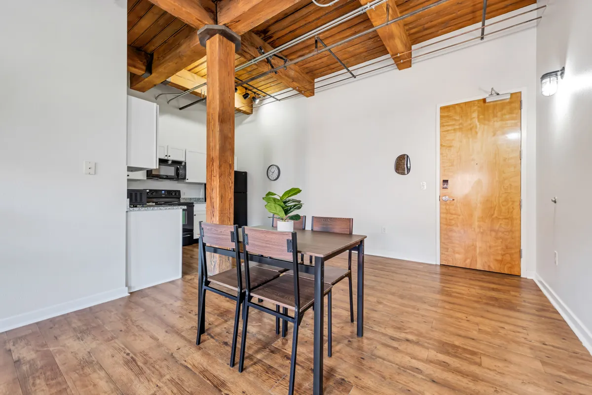 This image presents a welcoming dining area adjacent to the kitchen, framed by wooden beams and visible from the apartment’s front door. The well-appointed dining table encourages intimate dinners or casual weekday meals, reinforcing the space's role as a hub for togetherness.