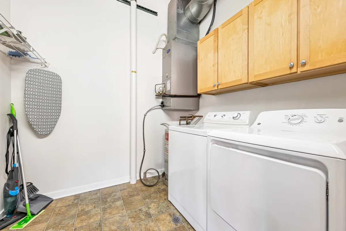 A tidy laundry area featuring a modern washing machine, dryer, storage cabinets, and an ironing board. The space is pristine and efficient, suggesting ease of living and thoughtful amenities.