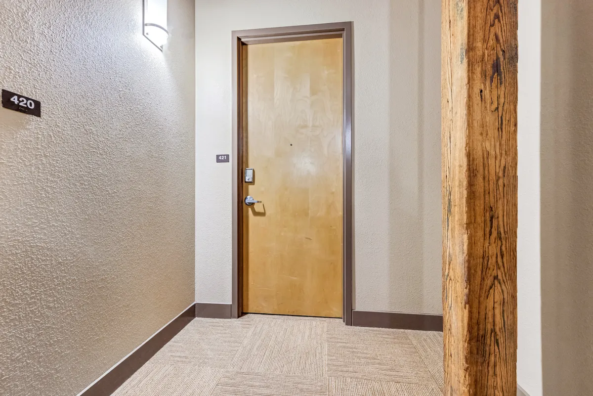 This image shows the entryway to two residences—door 421 and door 420—marked by a distinctive light fixture and a wooden structural beam. The composition captures the transition point between inside and outside, evoking a sense of arrival and community.